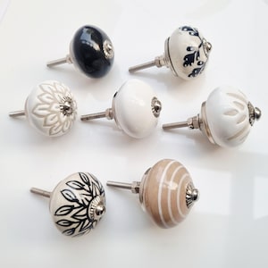 May include: A collection of ceramic cabinet knobs in various designs and colors. The knobs feature floral, striped, and solid patterns in black, white, and beige. Each knob has a silver-toned metal base and screw.