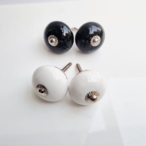 May include: Four decorative cabinet knobs. Two are glossy black, and two are glossy white. Each knob has a silver-colored, flower-shaped base. The knobs are oval-shaped and have a screw for attachment.
