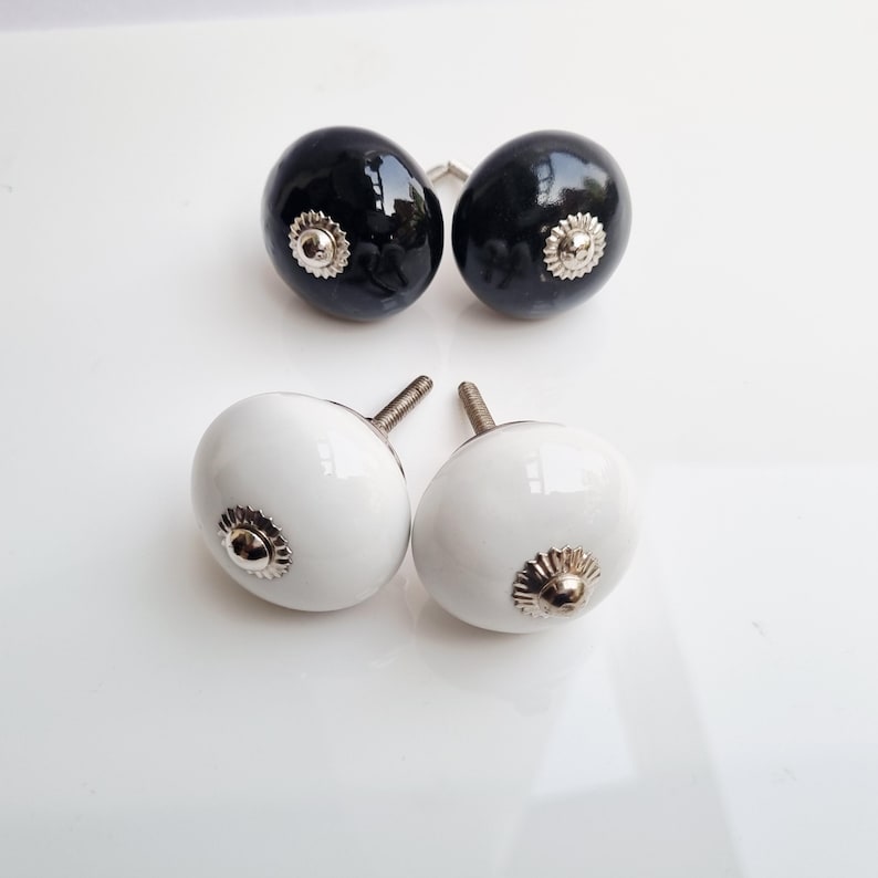 May include: Four decorative cabinet knobs. Two are glossy black, and two are glossy white. Each knob has a silver-colored, flower-shaped base. The knobs are oval-shaped and have a screw for attachment.