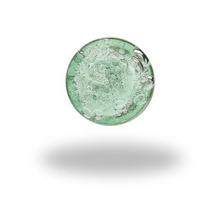 May include: A circular glass paperweight featuring a translucent light green tint. The interior of the glass is filled with numerous small, suspended air bubbles of varying sizes, creating a textured, effervescent appearance throughout the sphere.