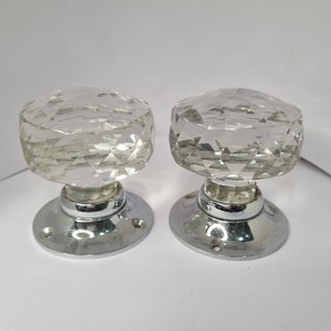 May include: Pair of clear glass door knobs with a faceted design. The knobs are mounted on chrome bases.
