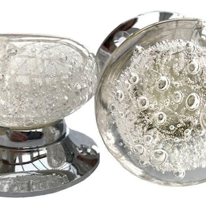 Könnte beinhalten: Zwei klare Glas-Türknäufe mit verchromter Basis. Das Glas hat eine blasenartige Textur.