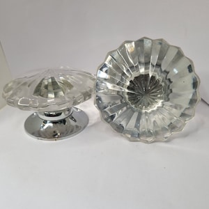 Pode incluir: Dois botões de porta de vidro transparente com um design facetado. Os botões têm uma base cromada.