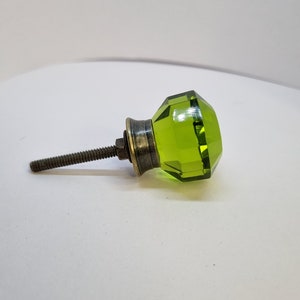 May include: A green glass cabinet knob with a faceted design and a brass screw.