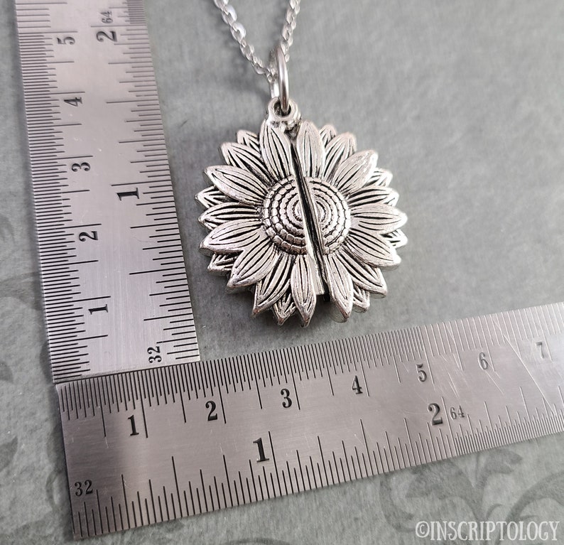 May include: Silver sunflower locket necklace with a chain. The locket is open and the two halves are separated. The locket is about 1 1/2 inches in diameter.