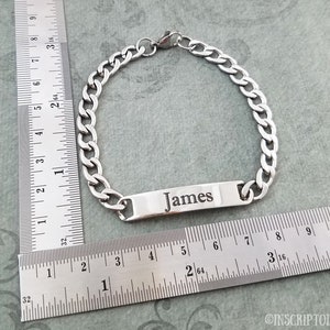 May include: A silver chain bracelet with a rectangular tag that says "James". The bracelet is measured against a ruler.