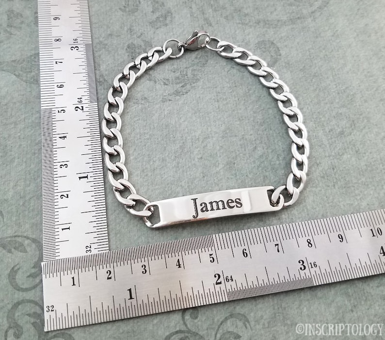 May include: A silver chain bracelet with a rectangular tag that says "James". The bracelet is measured against a ruler.