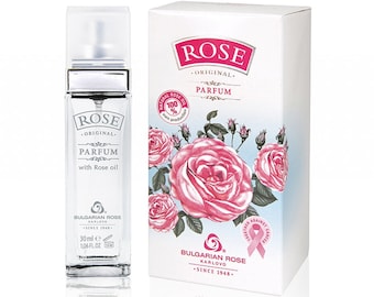 May include: A clear glass perfume bottle and a white box. The bottle has a silver cap and contains a liquid. The box features pink roses and the text "ROSE ORIGINAL PARFUM" and "BULGARIAN ROSE KARLOVO SINCE 1948".