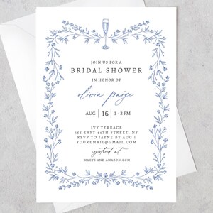 May include: A white bridal shower invitation with a blue floral border. The text reads "Join us for a Bridal Shower in honor of Olivia Paige Aug | 16 | 1-3PM Ivy Terrace 155 East 44th Street, NY RSVP to Jayne by Aug 1 youremail@gmail.com Registered at Macys and Amazon.com"