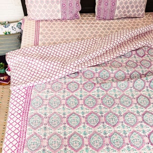 May include: A pink and white patterned quilt with a geometric design. The quilt is folded over a bed with matching pillowcases.