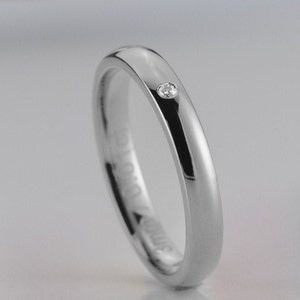 May include: A simple silver wedding band with a single small diamond set in the center.
