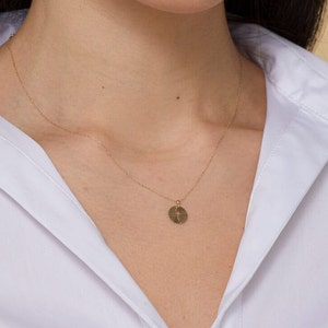 Puede incluir: Un collar de cadena de oro con un peque&ntilde;o colgante redondo con un dise&ntilde;o de cruz. El colgante tiene un patr&oacute;n texturizado en forma de sol.