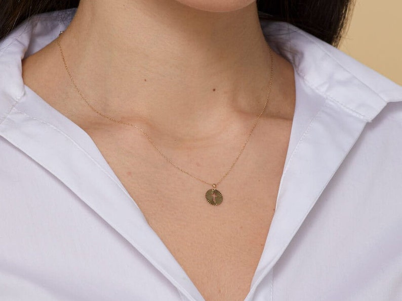 Puede incluir: Un collar de cadena de oro con un peque&ntilde;o colgante redondo con un dise&ntilde;o de cruz. El colgante tiene un patr&oacute;n texturizado en forma de sol.