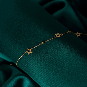 May include: A gold chain bracelet with star-shaped charms on a green fabric background.