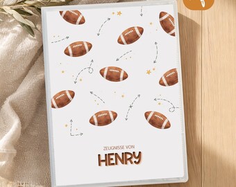 May include: A white binder featuring a repeating pattern of brown footballs, small yellow stars, and dashed directional arrows. The text "ZEUGNISSE VON HENRY" is printed in brown at the bottom centre of the cover, indicating a document holder.