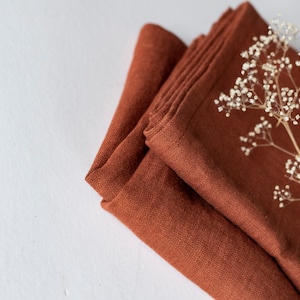 May include: A stack of rust-colored linen napkins with a sprig of white flowers on top.