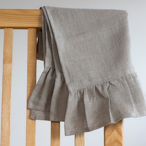 Può includere: Un asciugamano da tè in lino color beige chiaro con un bordo arricciato, appeso a una sedia di legno.