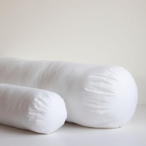 May include: Two white cylindrical pillows, one larger than the other, are placed side-by-side on a white surface.