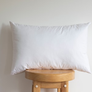 May include: A white pillow resting on a wooden stool. The pillow is plump and appears to be made of a soft material.