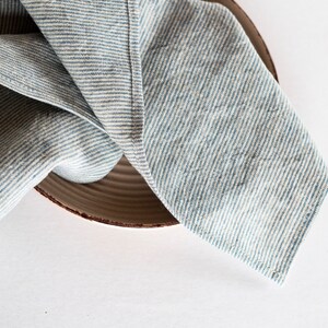 May include: A blue and white striped linen napkin is draped over a brown ceramic plate. The napkin's fabric has a textured appearance, with visible woven threads. The plate has a simple, rustic design.