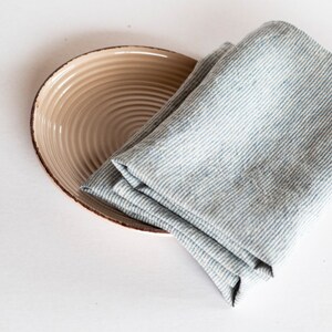 May include: A beige ceramic plate with a brown rim and a folded blue and white striped linen napkin. The plate has a ridged design. The napkin is folded and rests on the plate. The background is white.