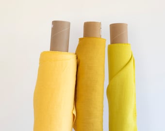 May include: Three rolls of yellow fabric, each a slightly different shade, are displayed on cardboard tubes against a white background.