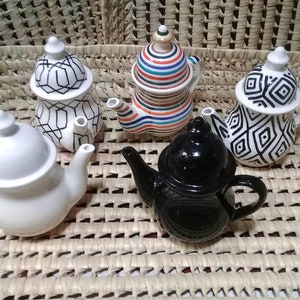 Peut inclure: Cinq théières en céramique de différentes couleurs et motifs. Les théières sont disposées dans un panier en osier. Les théières sont toutes de tailles et de formes différentes.