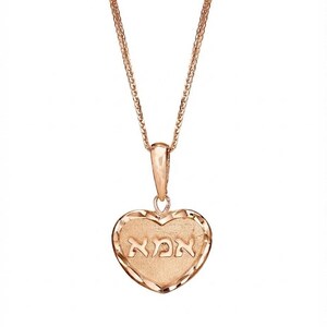 Puede incluir: Un collar con colgante en forma de coraz&oacute;n de oro rosa que presenta un centro texturizado con la palabra hebrea "אמא" grabada en el medio. El coraz&oacute;n tiene un borde facetado de corte diamante y cuelga de una delicada cadena de oro rosa.
