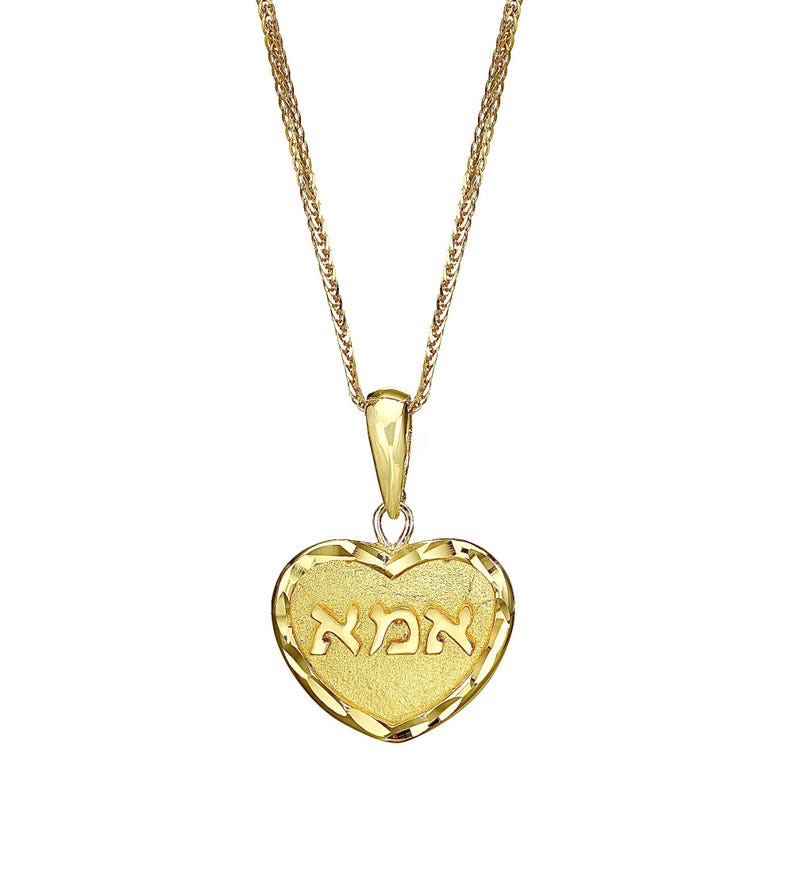 Puede incluir: Un collar con colgante en forma de coraz&oacute;n de oro que presenta un centro texturizado con la palabra hebrea "אמא" grabada en relieve. El coraz&oacute;n tiene un borde pulido y facetado, y cuelga de una delicada cadena de oro con una reasa.