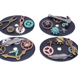 May include: Four black oval-shaped watch faces with various steampunk-style metal charms, including gears, a hammer, pliers, a feather, and a wrench.
