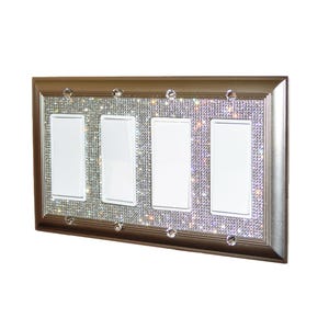 May include: A silver-colored light switch plate with four white switch covers. The plate is decorated with a sparkling, clear rhinestone design.