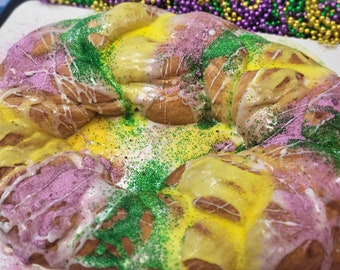 May include: A large, sweet, glazed pastry shaped like a ring, decorated with green, purple, and yellow sprinkles. The pastry is a traditional Mardi Gras treat.
