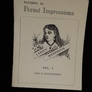 May include: A black and white illustration of a woman with a floral wreath and a banner that reads "Ladies' Workbook". The text "Patterns for Period Impressions Vol. 1 Lady's Accessories" is printed below the illustration.