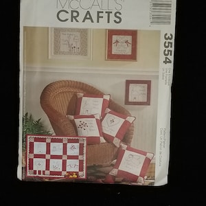 Op de afbeelding: Een McCall's Crafts naaipatroon voor een quilt en kussens. Het patroon bevat instructies voor het maken van een quilt met een rood-wit geruit patroon en acht verschillende geborduurde ontwerpen. De kussens zijn ook rood-wit geruit met geborduurde ontwerpen. Het patroonnummer is 3554.