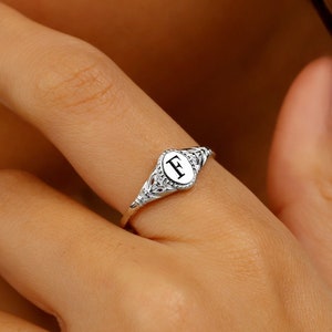 A silver signet ring with a white oval shaped stone featuring the letter 'F' in black.