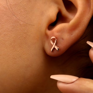A pair of rose gold stud earrings shaped like a ribbon.