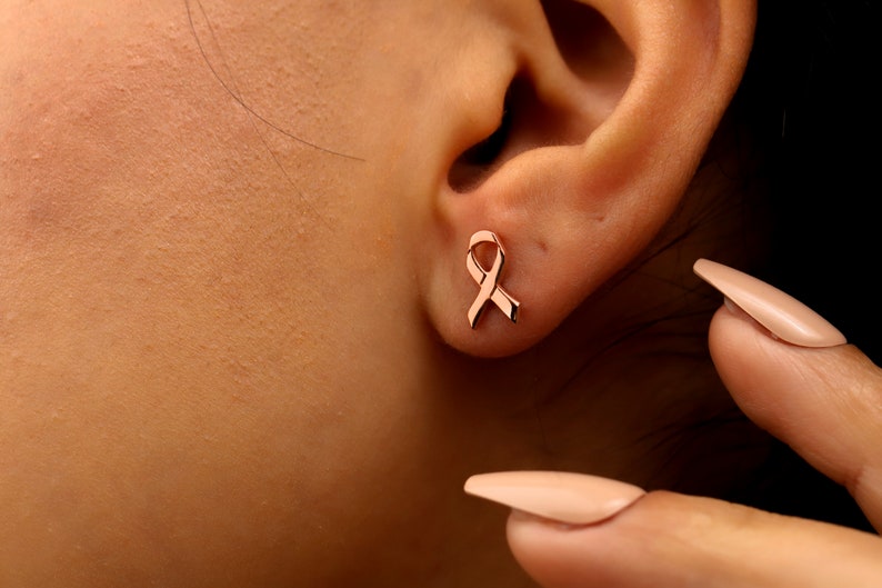 A pair of rose gold stud earrings shaped like a ribbon.