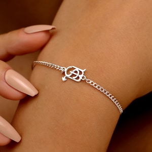 May include: A silver bracelet with a chain link design. The bracelet features a decorative centerpiece with an arrow and the letters "G" and "B". The bracelet is on a person's wrist.
