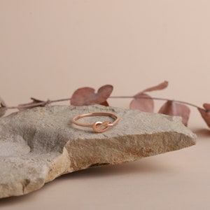 A rose gold knot ring on a light brown rock. The ring is simple and delicate.