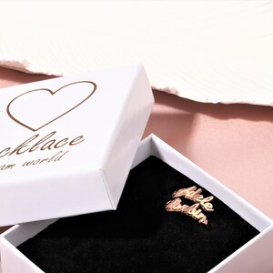 A white box with a heart and the text 'necklace dream world' on the lid. The box is open and a gold necklace with the names 'Adele' and 'London' is inside.