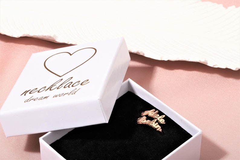 A white box with a heart and the text 'necklace dream world' on the lid. The box is open and a gold necklace with the names 'Adele' and 'London' is inside.