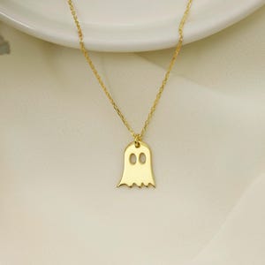 A gold chain necklace with a gold ghost pendant. The ghost has two small circles for eyes.