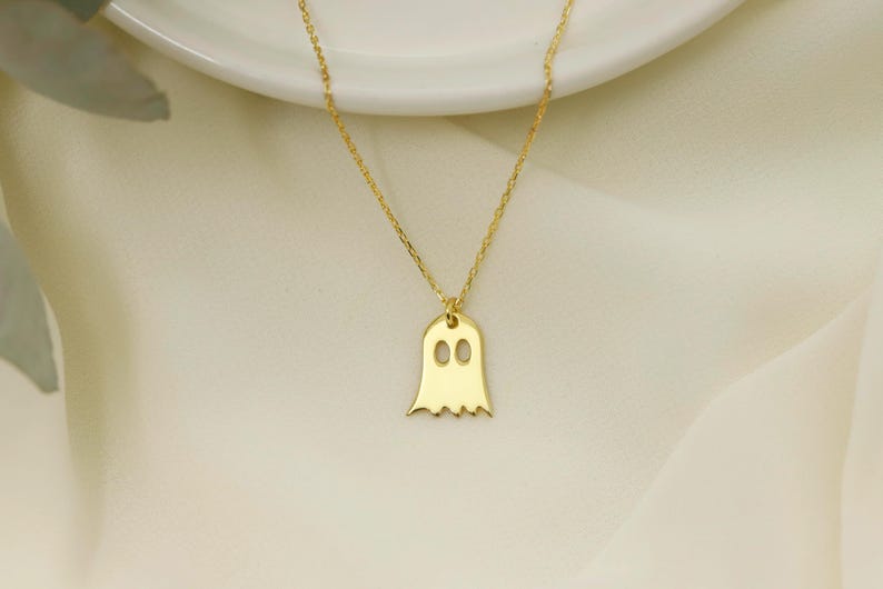 A gold chain necklace with a gold ghost pendant. The ghost has two small circles for eyes.