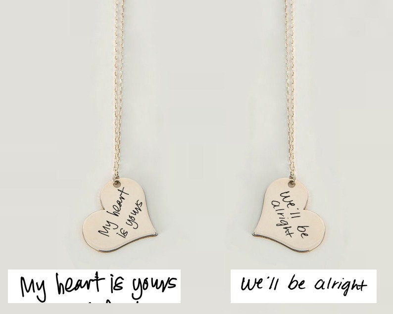 Two gold heart-shaped necklaces with handwritten messages. The necklace on the left has the message 'My heart is yours' and the necklace on the right has the message 'We'll be alright'.