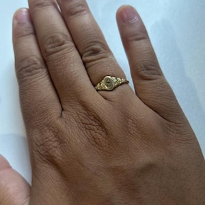 A gold ring with an oval-shaped setting featuring the letter 'S' in black lettering.
