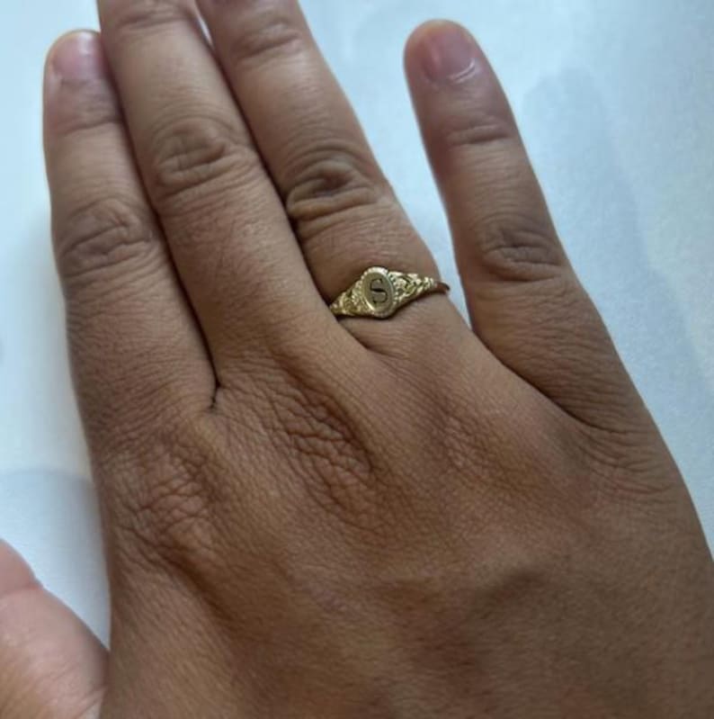 A gold ring with an oval-shaped setting featuring the letter 'S' in black lettering.