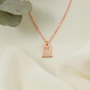 A rose gold chain necklace with a ghost pendant. The pendant is a simple outline of a ghost with two small circles for eyes.