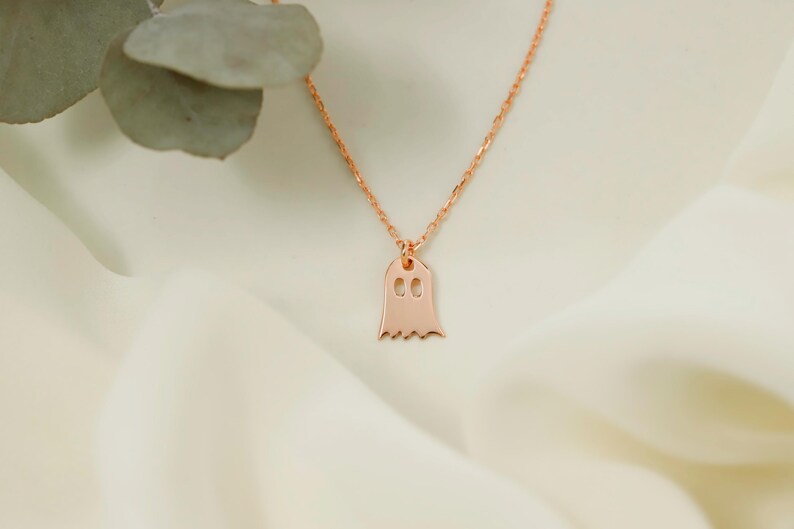 A rose gold chain necklace with a ghost pendant. The pendant is a simple outline of a ghost with two small circles for eyes.