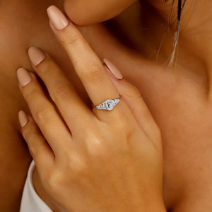 A silver signet ring with a raised letter 'F' in the center. The ring is set with small, clear stones around the letter.