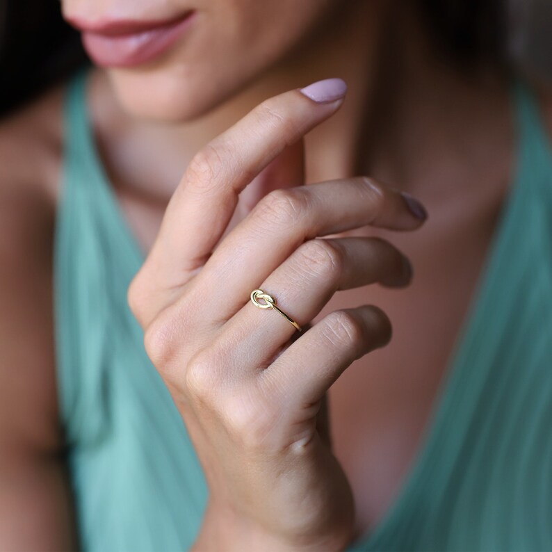 A gold knot ring with a simple design. The ring is worn on the finger of a person's hand.